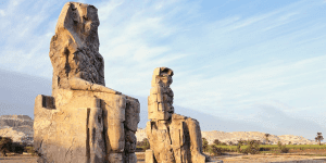 The two massive quartzite statues, the Colossi of Memnon, silhouetted against a golden-hour sky in Luxor, during an expert-guided private tour with Top Class Egypt Travel.