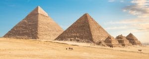 A wide panoramic view of the Great Pyramids of Giza and the Queens' Pyramids with camels in the desert, part of a private luxury itinerary by Top Class Egypt Travel.
