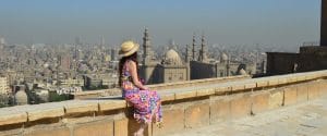 A woman in a sun hat sitting on a stone wall overlooking the domes and minarets of Islamic Cairo. - Saladin Citadel of Cairo