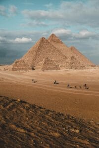 Side view of the Great Pyramids of Giza in the desert landscape, showcasing the massive scale of the limestone blocks under a clear sky.