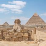 The Great Sphinx of Giza with the Great Pyramid of Khufu in the background under a clear blue sky, Cairo, Egypt.