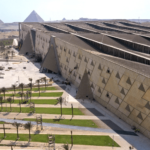 An aerial view of the modern Grand Egyptian Museum (GEM) complex with the Giza Pyramids in the background, a premier stop on private tours by Top Class Egypt Travel.