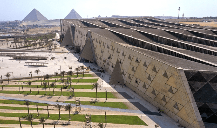An aerial view of the modern Grand Egyptian Museum (GEM) complex with the Giza Pyramids in the background, a premier stop on private tours by Top Class Egypt Travel.