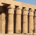 A close-up view of a row of massive, ancient stone columns with papyrus-shaped capitals at Karnak Temple in Luxor, showcasing the grand scale of ancient Egyptian architecture under a clear sky.