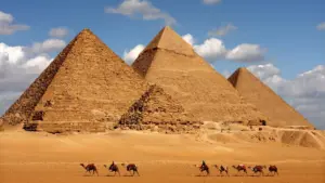 A line of camels walking across the sand in front of the Pyramids of Giza, Egypt