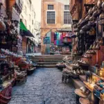 A view through a historic stone archway into a bustling alley of Khan El-Khalili bazaar in Cairo, filled with glittering traditional lanterns, brassware, and colorful artisanal crafts.