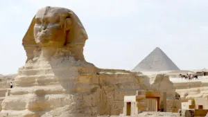 Side profile view of the ancient Great Sphinx of Giza with a stone pyramid rising in the background.