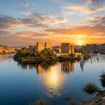 Philae Temple dedicated to goddess Isis on a serene island in the Nile River near Aswan Egypt at golden sunset with felucca boats sailing around it