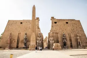 The grand entrance pylon of Luxor Temple with ancient stone obelisks and statues under a bright sky.