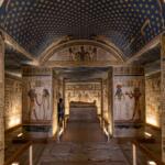 An interior view of a royal ancient Egyptian tomb in the Valley of the Queens, showcasing a star-patterned vaulted ceiling and masterfully preserved, colorful hieroglyphics.