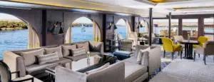 Modern cruise salon with long upholstered sectional sofas and arched windows overlooking the Nile