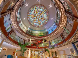 Upward perspective of a circular multi-level cruise atrium crowned by an ornate stained-glass dome skylight