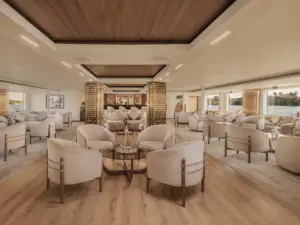 Opulent cruise salon lounge with cream tub armchairs, wood paneled ceilings, gold pillars, and evening lighting