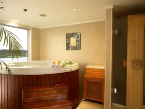 Round wooden-paneled whirlpool jacuzzi tub, sauna door, and window inside a tiled spa room