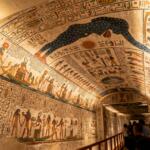 An interior view of an Egyptian tomb featuring an arched ceiling decorated with blue-skinned deities and golden stars.