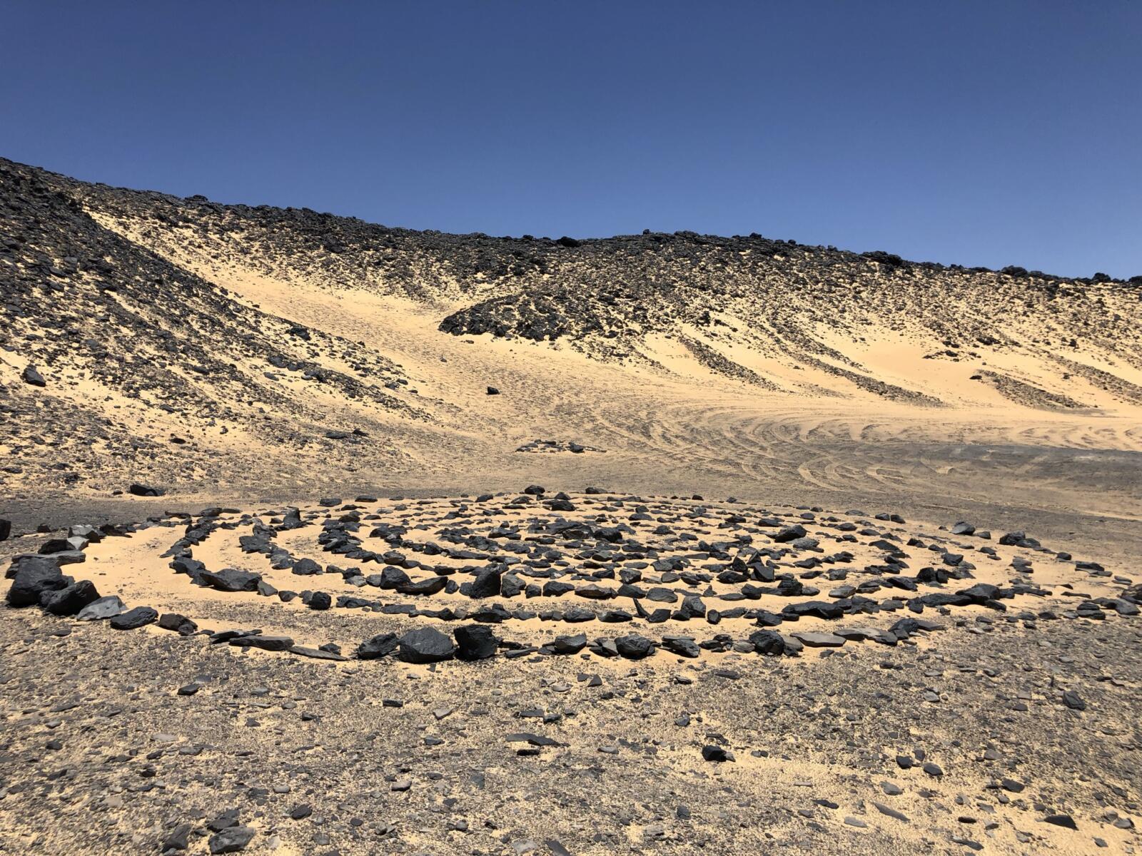 A spiral pattern made of dark volcanic stones laid on the sand in the Black Desert, Egypt