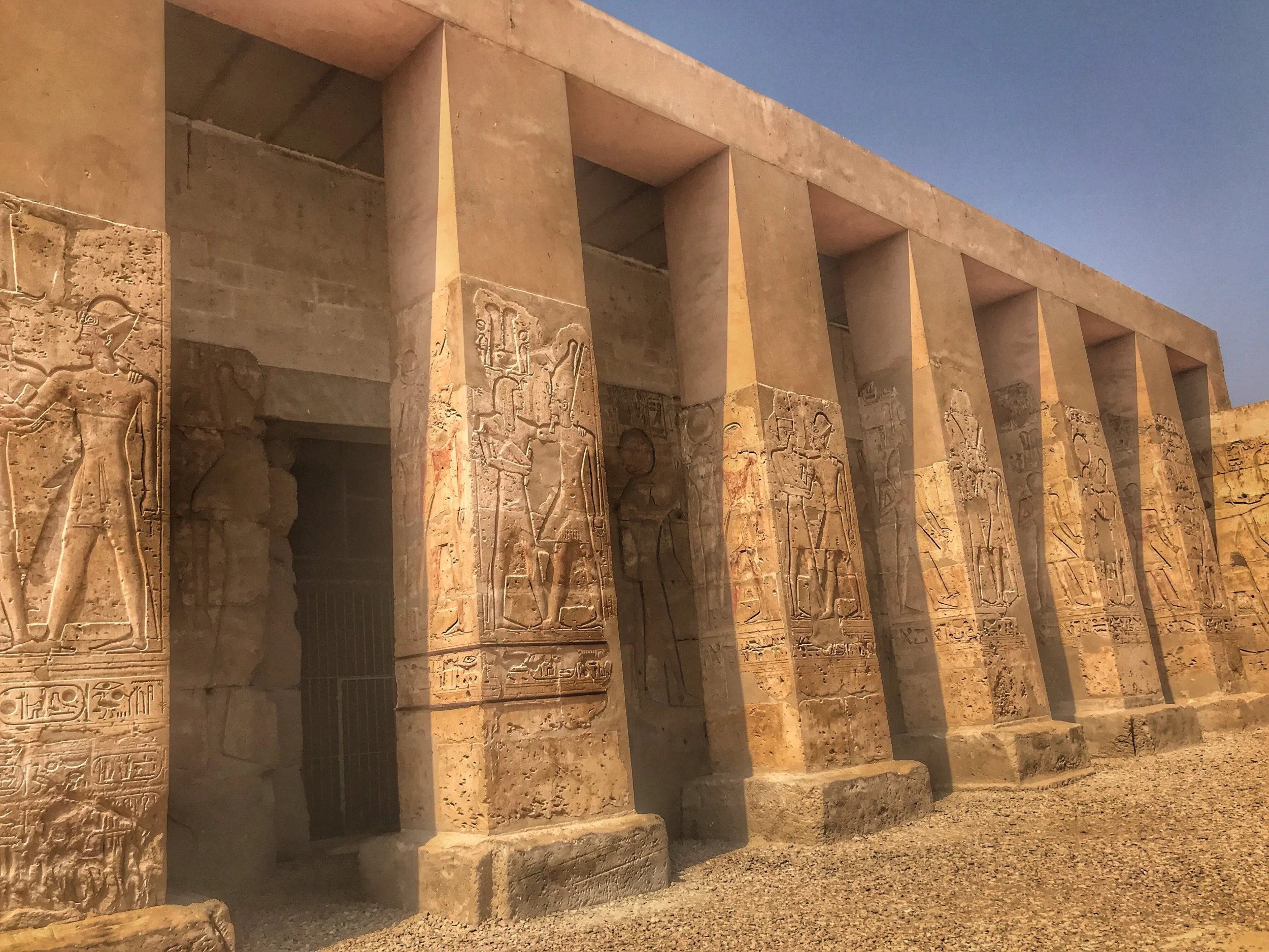 Detail view of the massive stone columns and intricate relief carvings at the Temple of Abydos, Egypt, featuring strong side lighting and a perspective view, as seen on a Top Class Egypt Travel private excursion.
