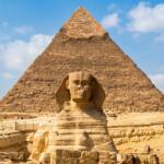 The Great Sphinx statue in front of the ancient Pyramid of Khafre under a blue sky in Giza, Egypt.