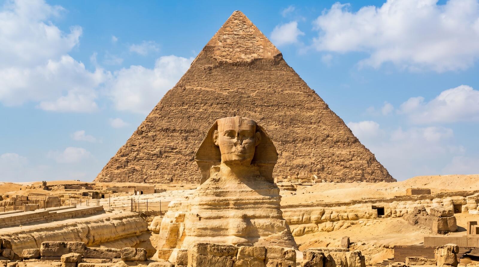 The Great Sphinx statue in front of the ancient Pyramid of Khafre under a blue sky in Giza, Egypt.
