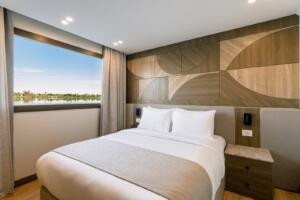 Close view of comfortable double bed with white linens and bedside table inside Jubal Dahabiya luxury cabin